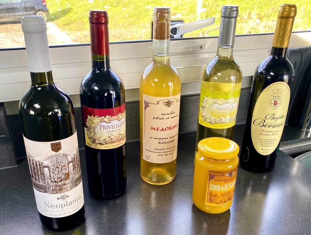 A collection of six different bottles of wine and a jar of honey on a kitchen countertop. The wines include red and white varieties with labels in various languages, along with a distinctive jar of honey.