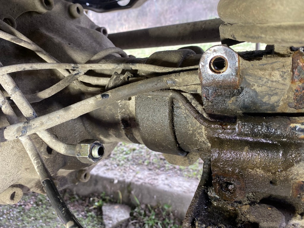 Close-up view of a dirty mechanical component with pipes and fittings, showing signs of oil and grime buildup.