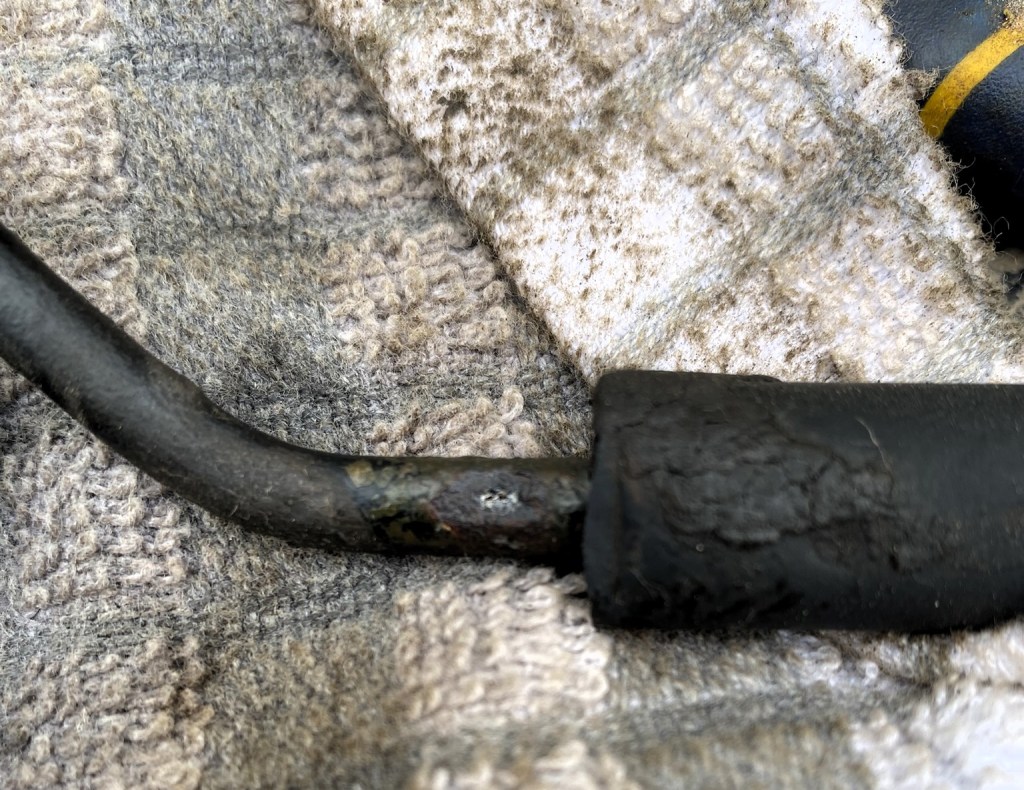 A close-up of a worn and slightly corroded black cable resting on a textured, dirty cloth.