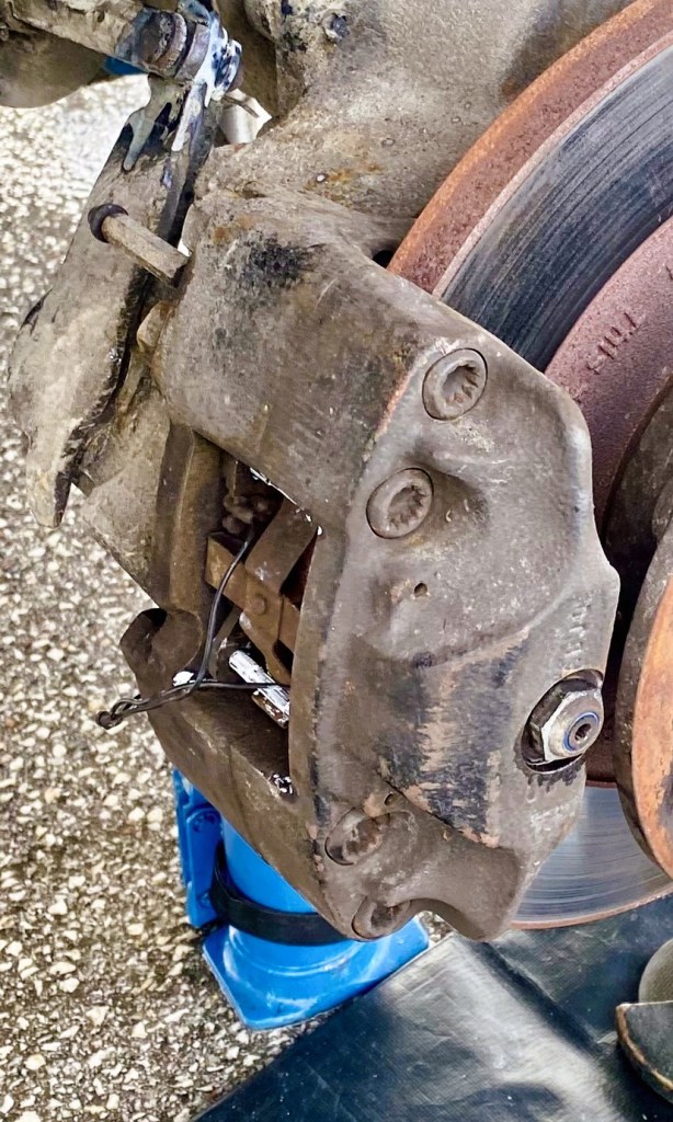 Close-up view of a car brake caliper and disc, showing wear and dirt on the components.