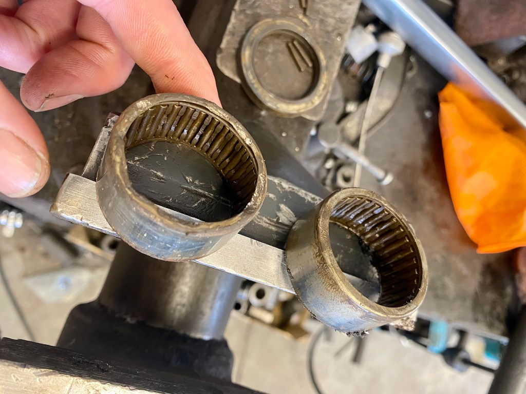 A close-up of a hand holding a metallic component with two circular bearing races, placed on a workbench covered with tools.