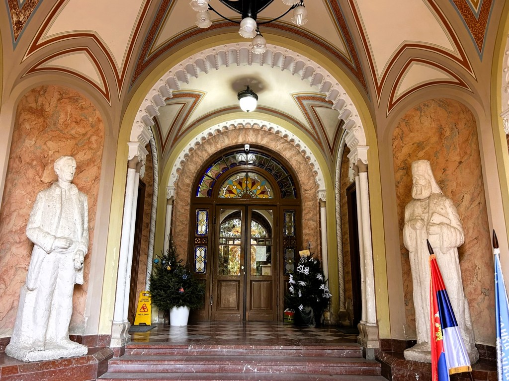 The entrance hall featuring ornate architecture, two statues on either side, and a decorated Christmas tree.