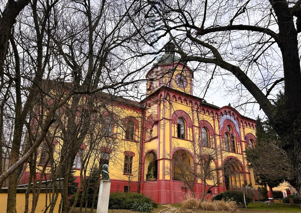 A historic building with a yellow and red façade, featuring arched windows and a clock tower, surrounded by bare trees.