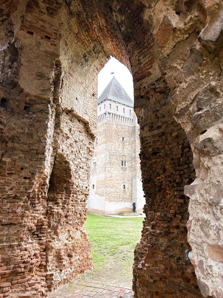 View through a brick archway revealing a medieval tower and grassy courtyard.