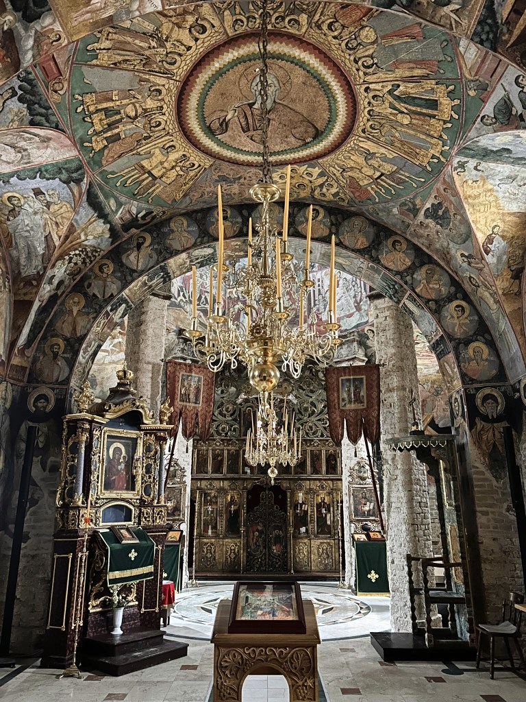 Interior view of an ornate church featuring a decorative chandelier, elaborate frescoes on the ceiling and walls, and a wooden altar adorned with religious icons.