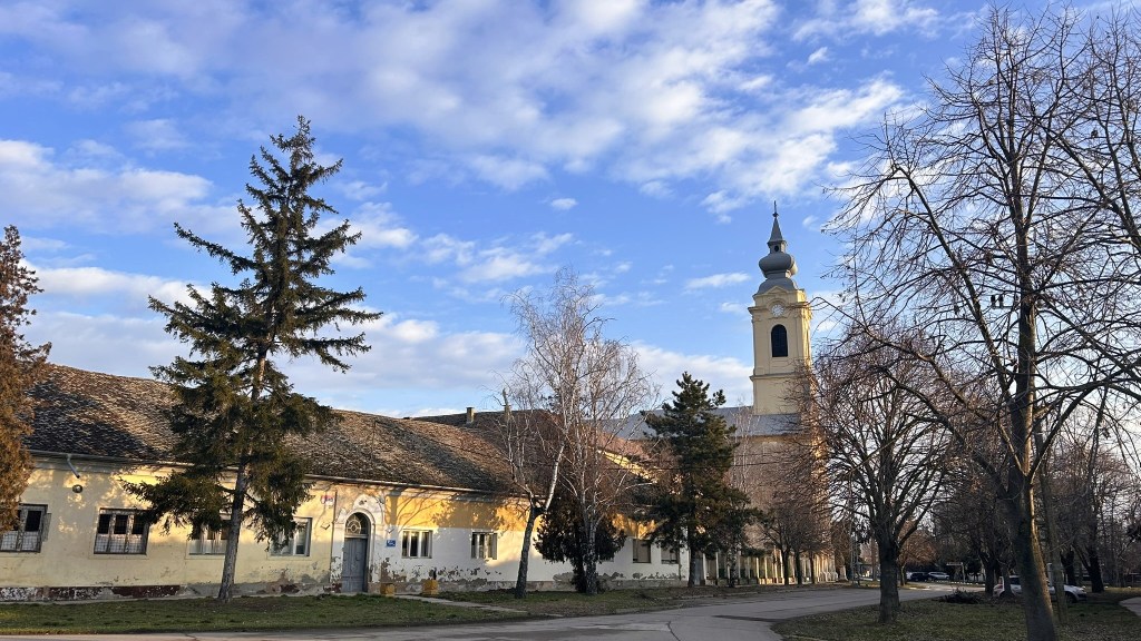 A view of a historic building with a bell tower, surrounded by trees and a clear blue sky.