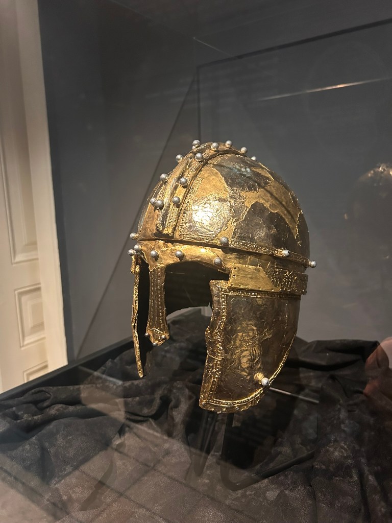 Ancient golden helmet displayed in a glass case, featuring intricate designs and metal embellishments.