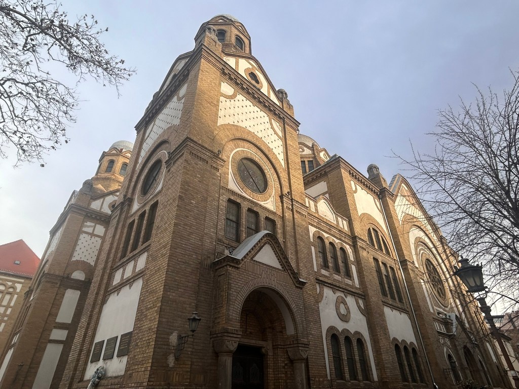 Side view of a historical brick building with arched windows and domed rooftops, against a cloudy sky.