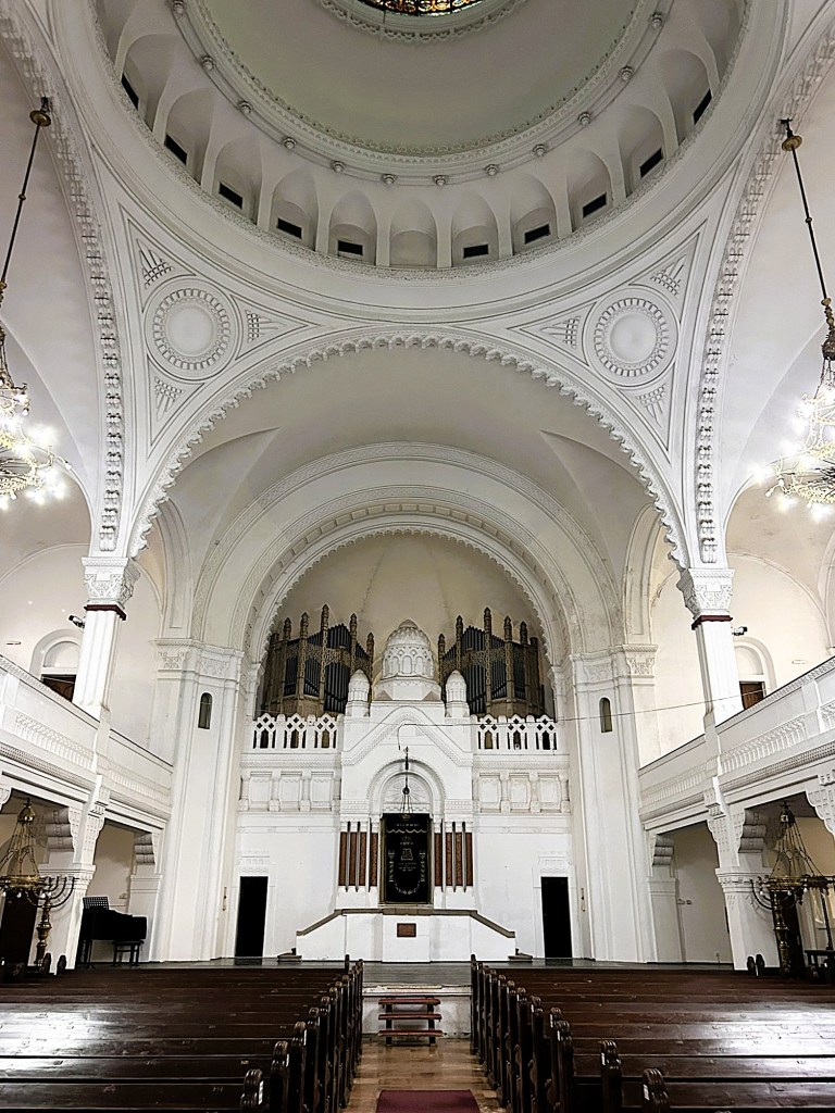 Interior view of a decorated church featuring a high ceiling with intricate designs, an organ at the altar, and rows of wooden pews.