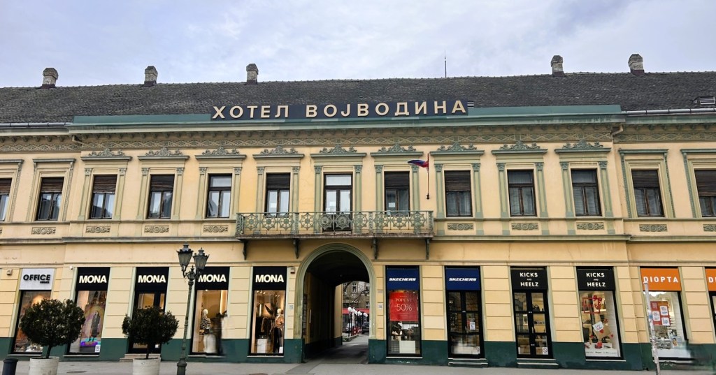 Facade of Hotel Vojvodina with a decorative balcony and storefronts below, located in a historic building.