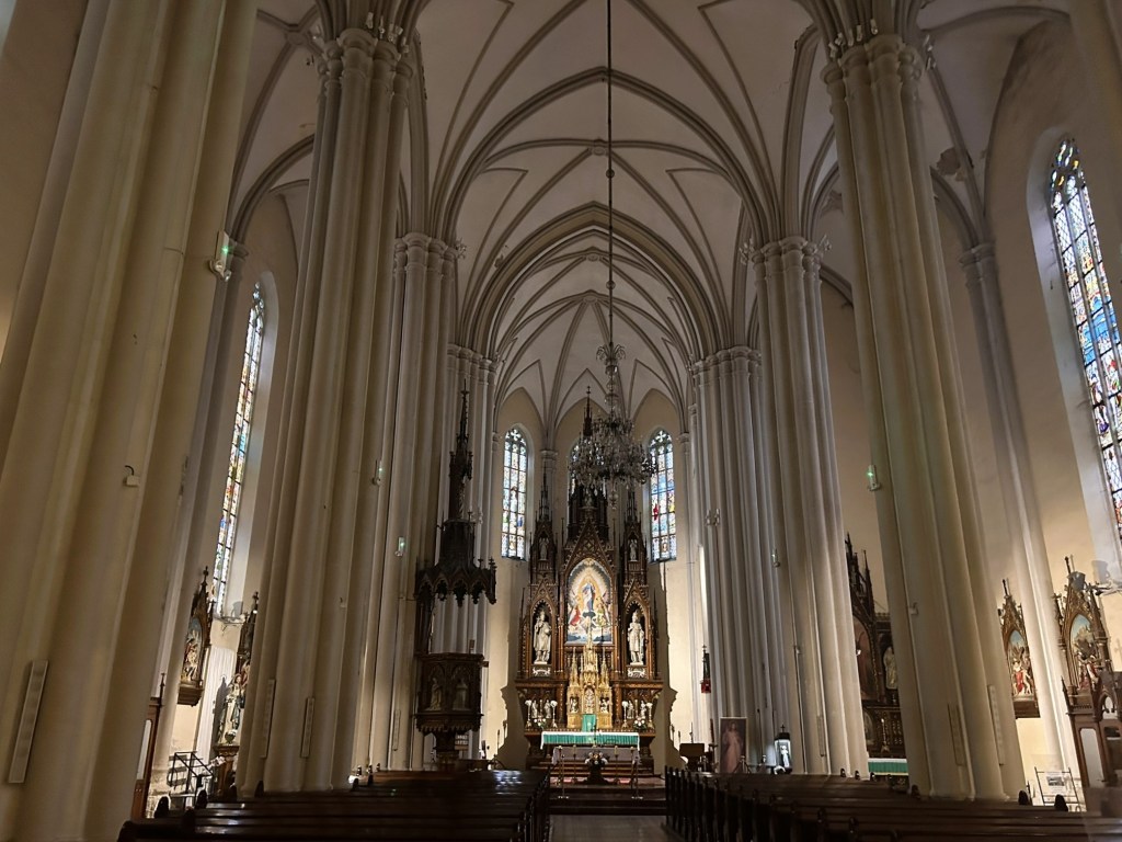 Interior view of a church featuring tall columns, ornate altar, and stained glass windows.
