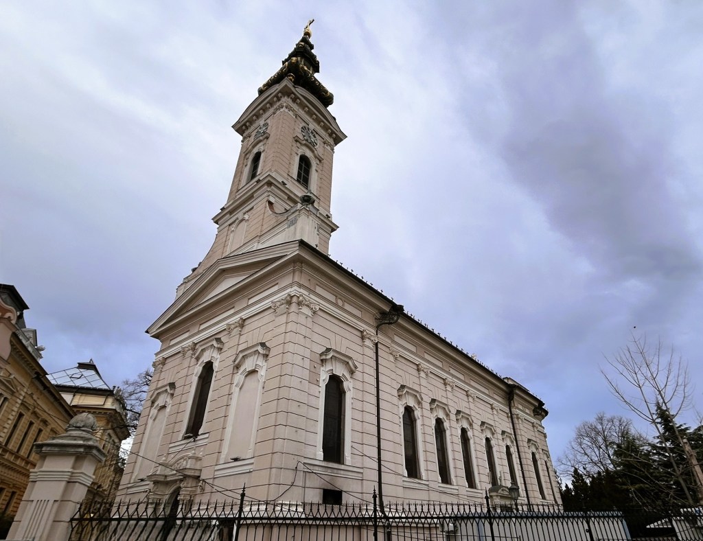 Side view of a historical building featuring a tall clock tower, ornate architecture, and a cloudy sky in the background.