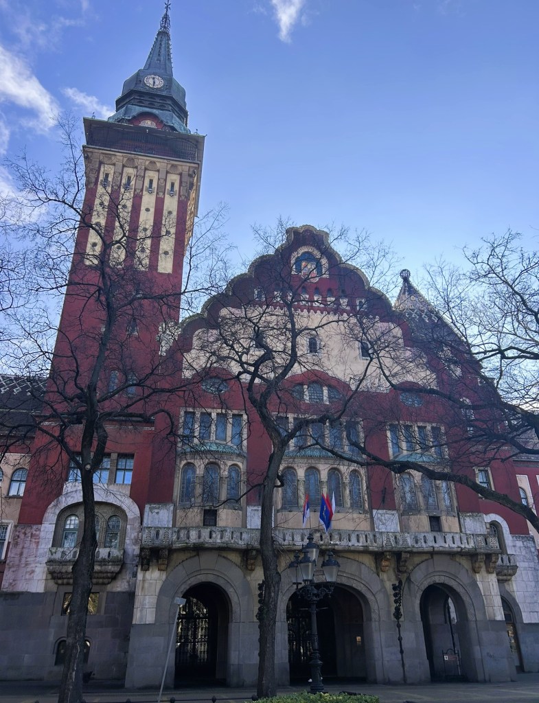 Historic building featuring a tall clock tower and ornate façade, surrounded by bare trees and a clear blue sky.