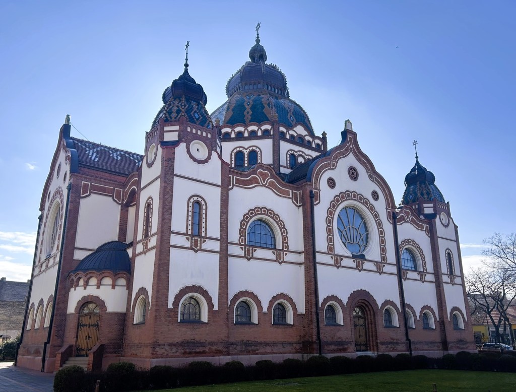 A side view of a grand building featuring intricate architectural details, domes, and large arched windows, set against a clear blue sky.