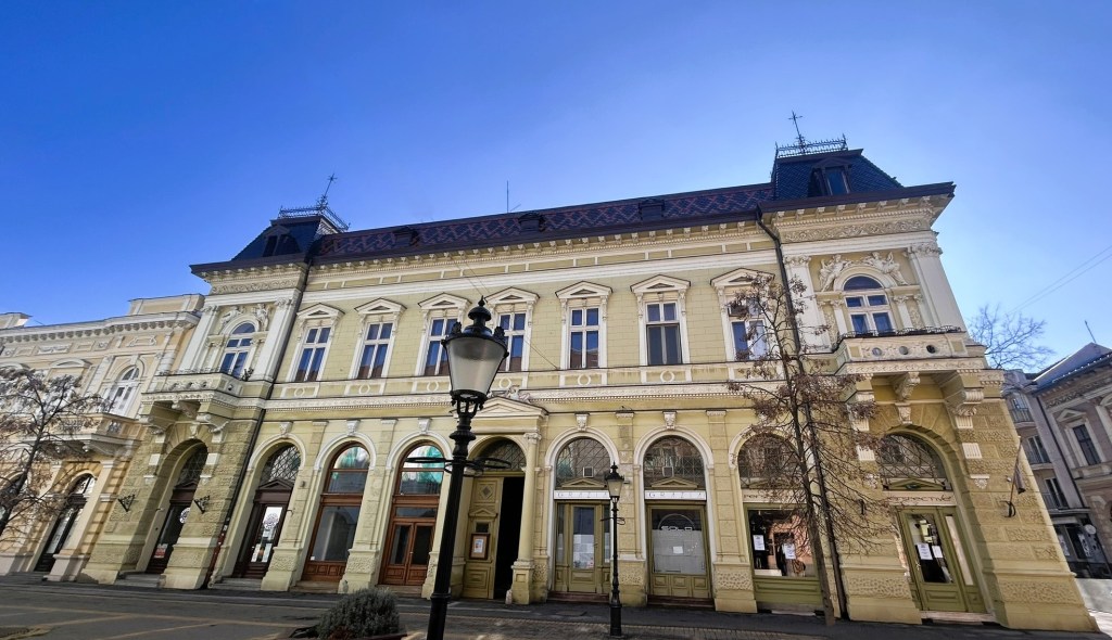 Historic yellow building with ornate architectural details and arched windows, featuring a lamp post in front against a clear blue sky.