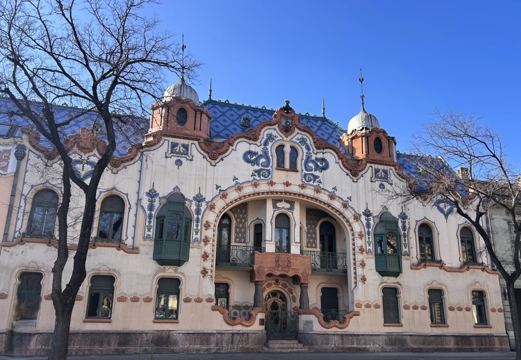 Ornate architectural building featuring colourful tiles, decorative elements, and intricate details against a clear blue sky.