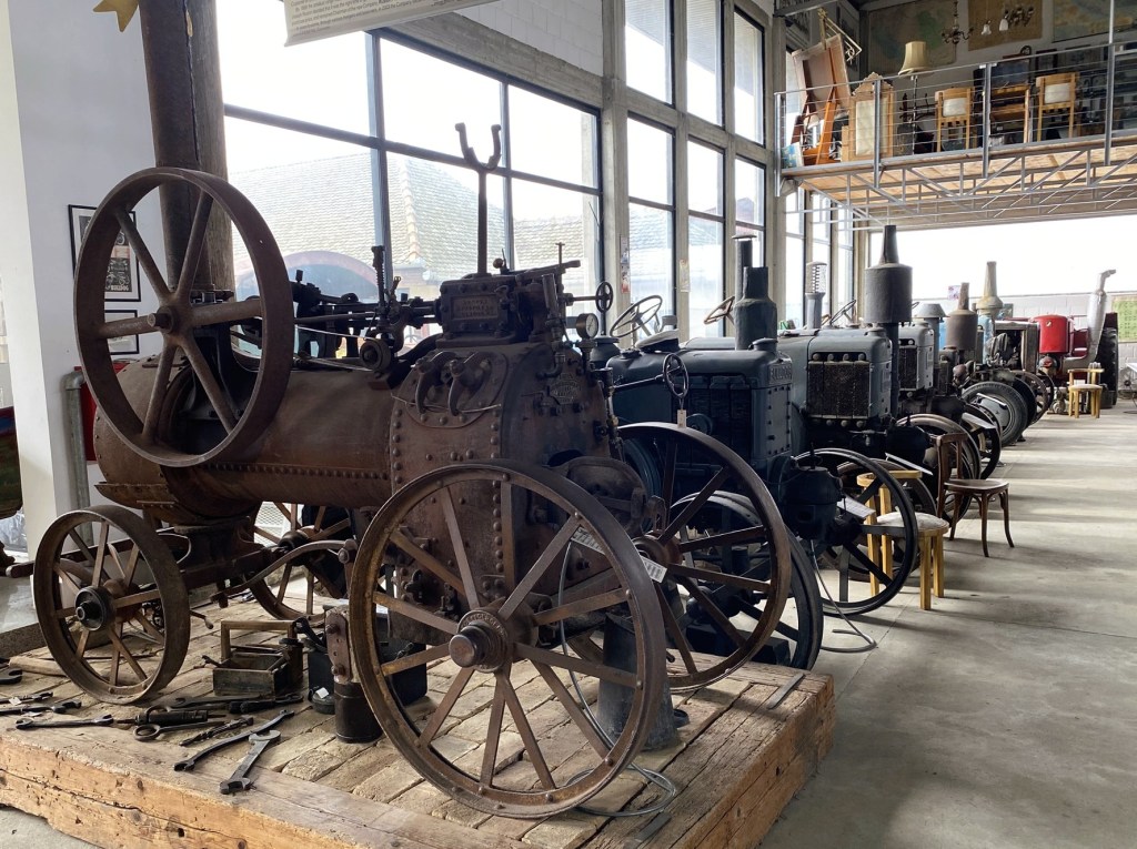 Historical agricultural machinery displayed in a museum, featuring various antique tractors and tools along with a spacious industrial setting.