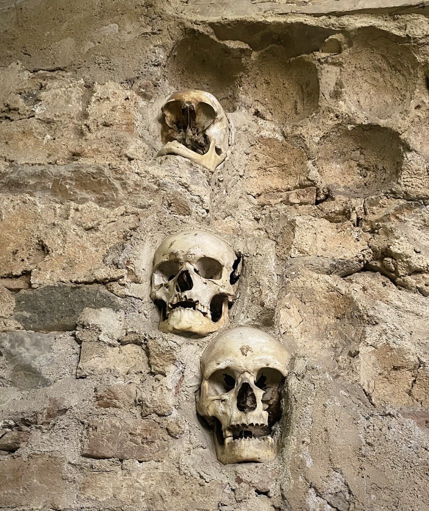 Three human skulls embedded in a stone wall with a rustic texture.