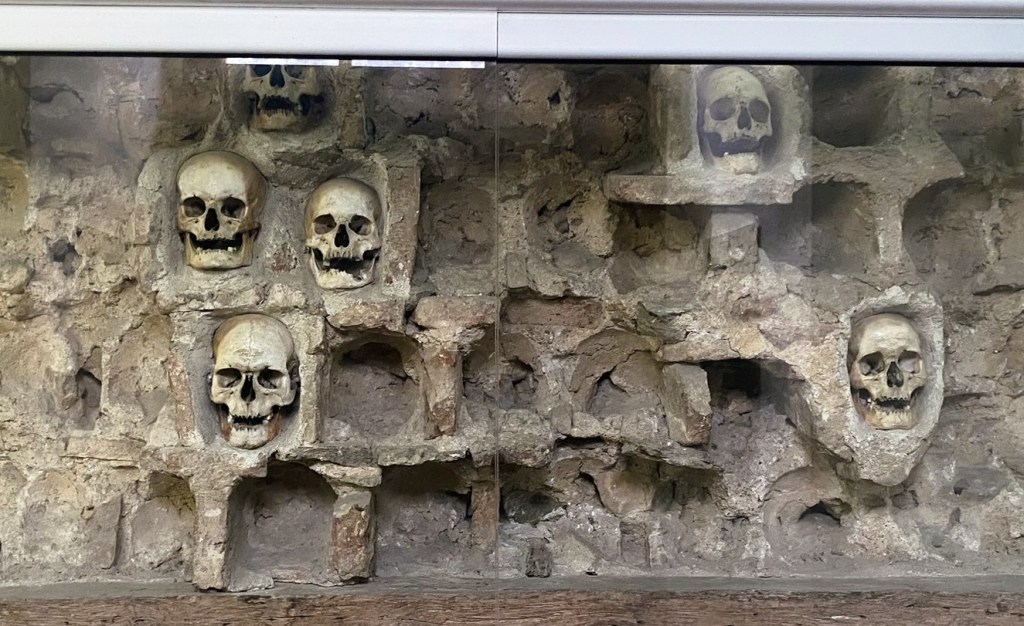 A display of human skulls arranged in recesses within a stone wall, showcasing a historical or archaeological context.