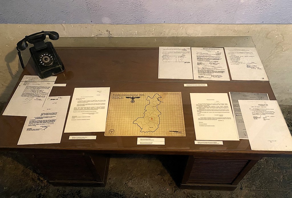 A vintage black rotary telephone on a table surrounded by various documents, including maps and letters, displayed under glass.