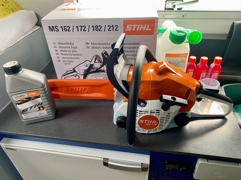 A STIHL MS 172 chainsaw on a worktop, accompanied by a bottle of STIHL ForestPlus oil, a spare chain and several bottles of oil in the background, alongside a product box.