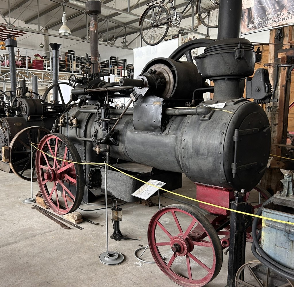 A vintage steam engine displayed in a museum, featuring large red wheels, black machinery, and various components typical of early industrial technology.
