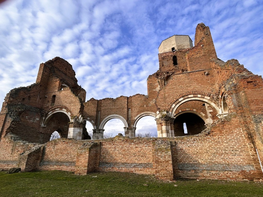 Ruined brick structure with arched windows and a partially collapsed tower, set against a cloudy sky.