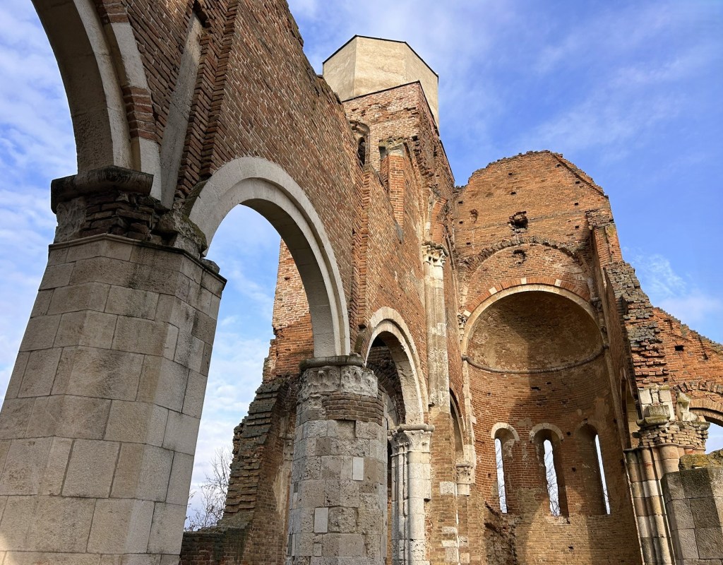 Ruins of an ancient brick structure with arches and stone walls, set against a blue sky.