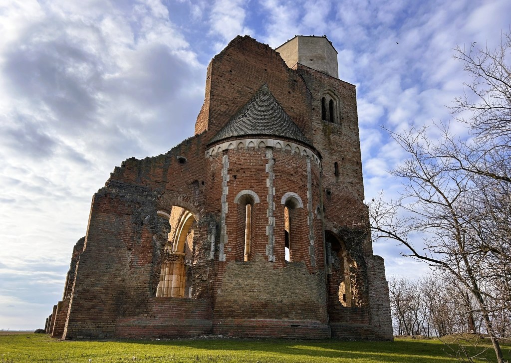 Ruined brick church with a tower, set against a cloudy sky.