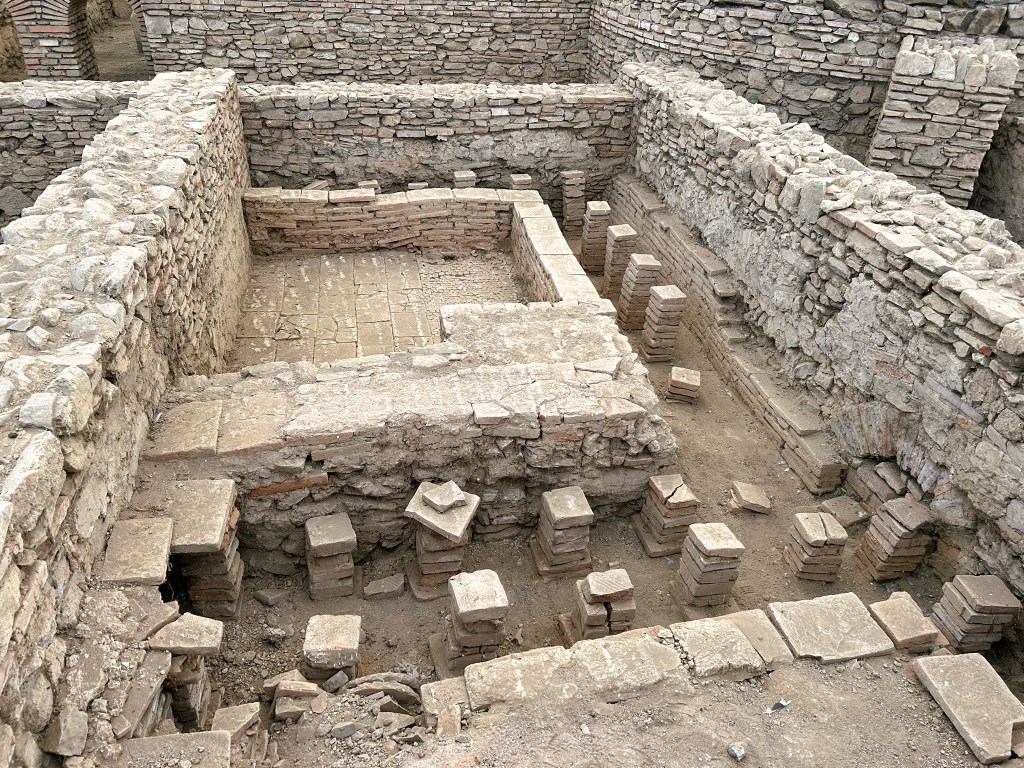 An archaeological site featuring ancient stone foundations and walls, with a layout including a rectangular structure and various stacked stone blocks.
