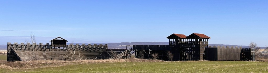 A wooden fort with high walls and two towers under a clear blue sky.