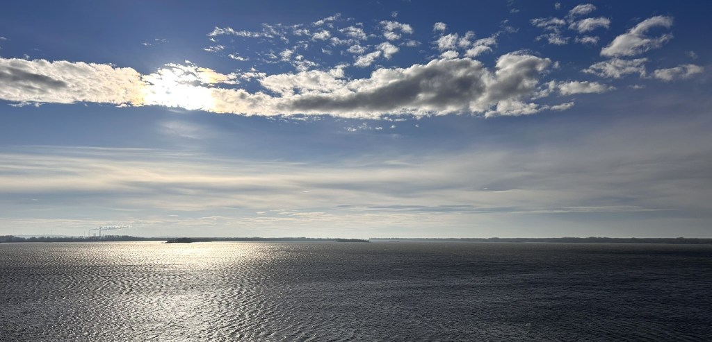 A serene view of a tranquil body of water under a partly cloudy sky, with sunlight reflecting on the water's surface.