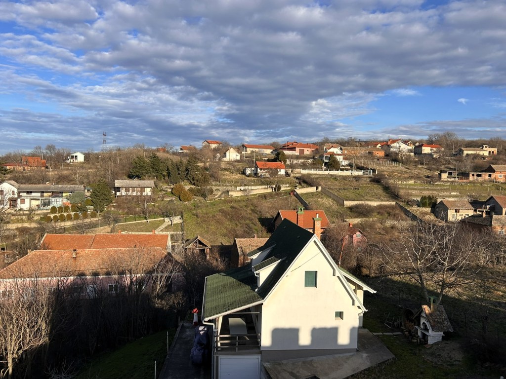A panoramic view of a rural landscape featuring houses on hills under a partly cloudy sky.