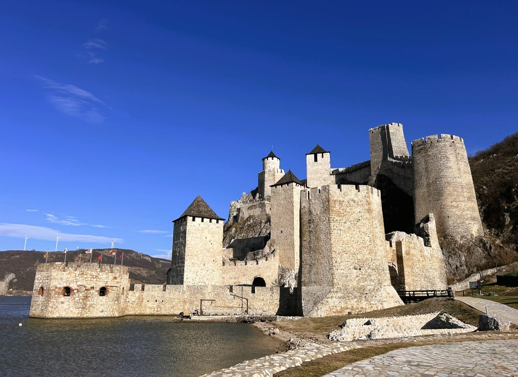 A historic stone castle situated by the water, featuring multiple towers and surrounding walls under a clear blue sky.