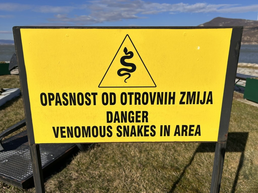 Warning sign indicating the presence of venomous snakes in the area, featuring a snake symbol and text in both Croatian and English.