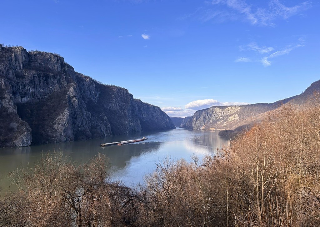 A scenic view of a winding river flanked by tall cliffs under a clear blue sky, with a barge navigating the water.