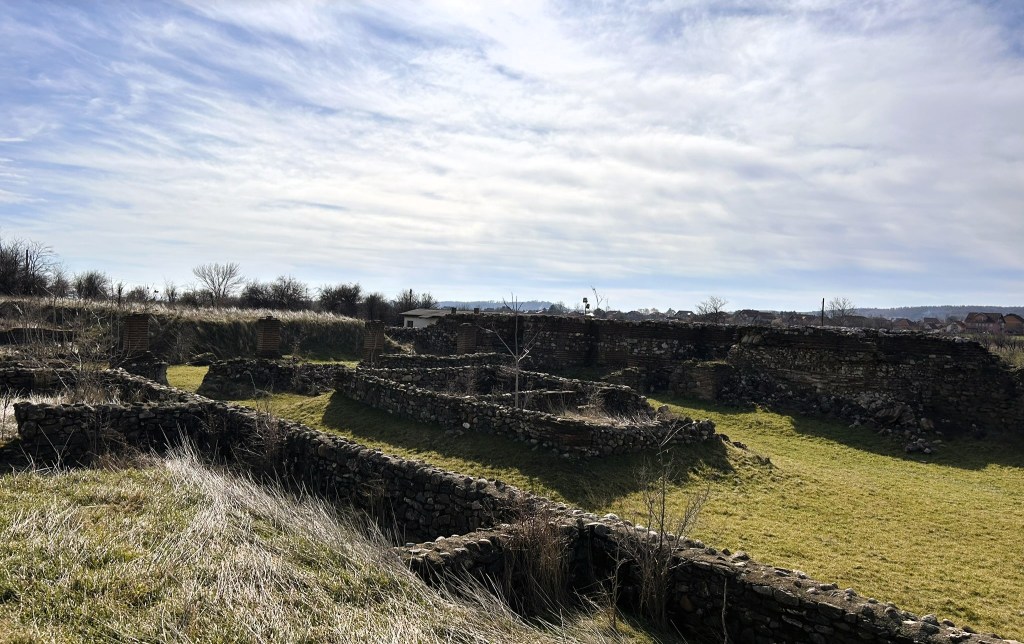 Remains of stone structures in a grassy area under a cloudy sky.