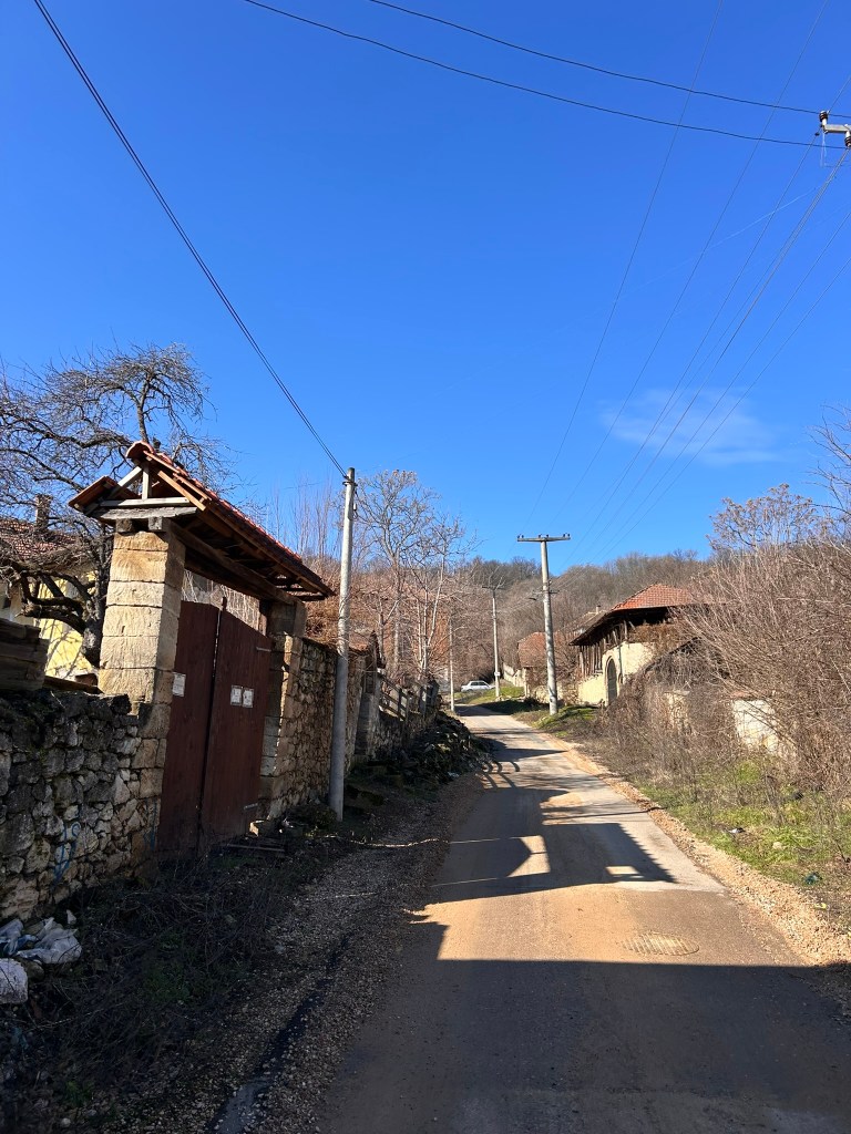 A quiet rural road lined with stone walls and wooden gates, under a clear blue sky.