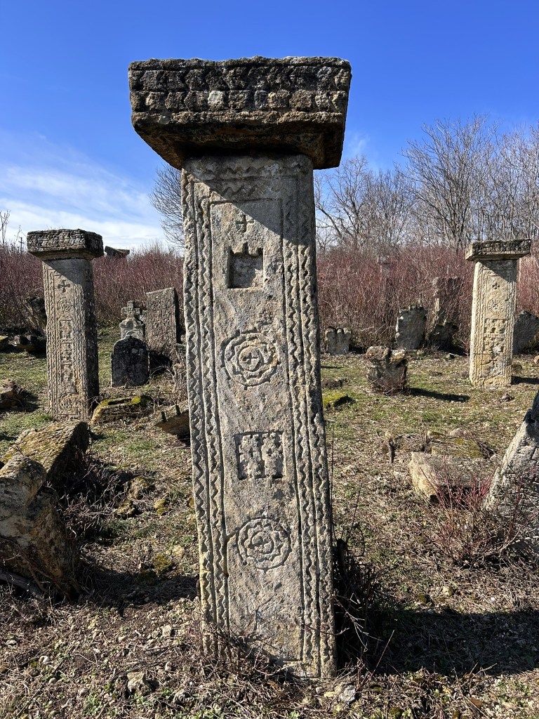 Ancient stone pillars with intricate carvings in a grassy field under a blue sky.