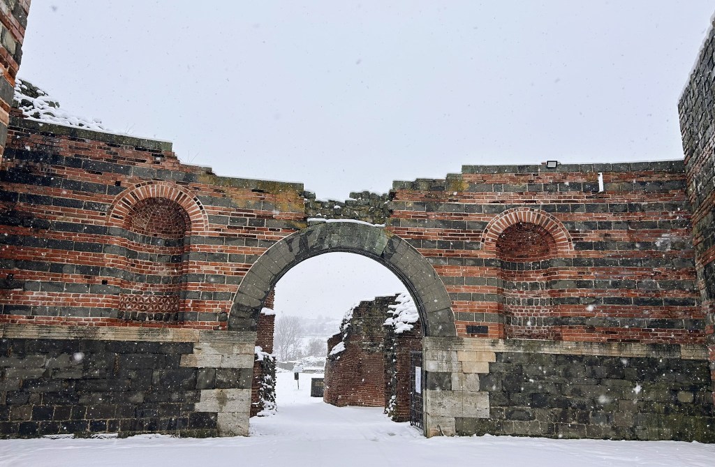 Snow-covered ruins featuring a large archway surrounded by brick and stone walls.