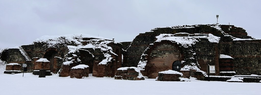 Snow-covered ruins of an old stone structure with arched openings, surrounded by a snowy landscape.