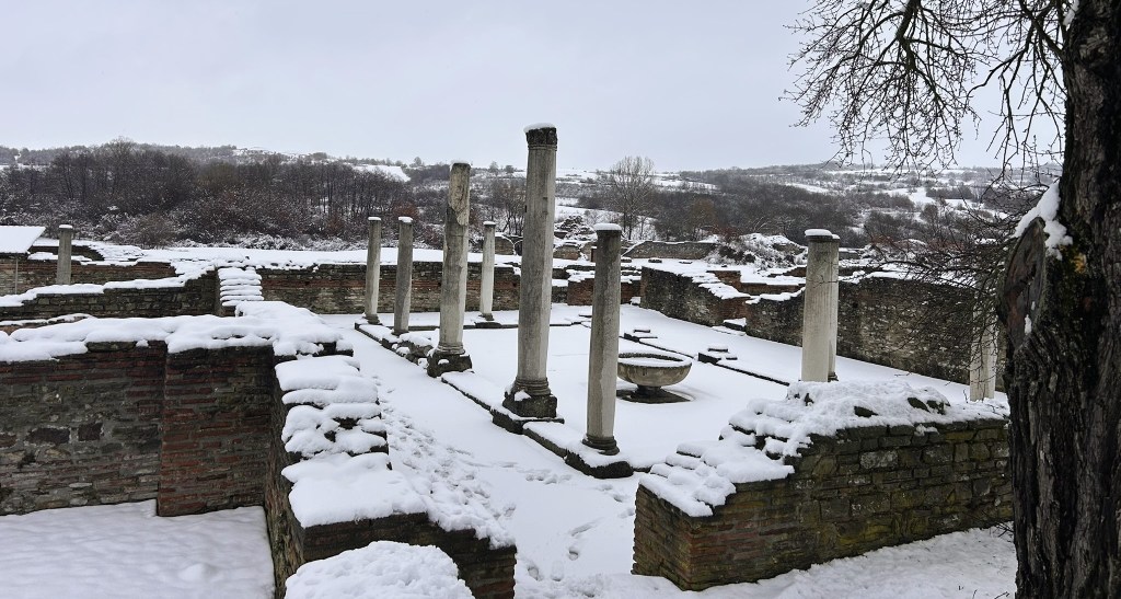 Snow-covered ancient ruins with several columns and stone walls, set against a winter landscape.