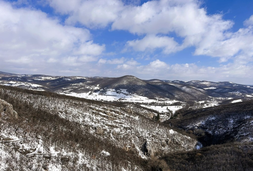 Panoramic view of snow-covered hills and valleys under a partly cloudy sky.
