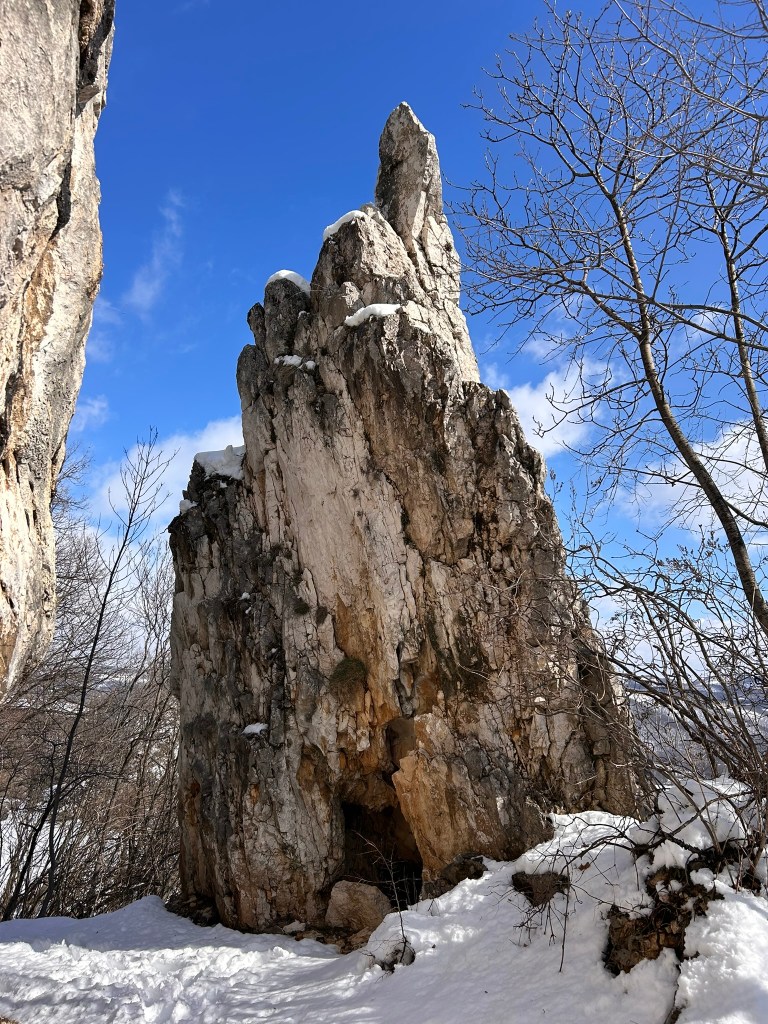 A tall rock formation covered in snow, surrounded by sparse trees under a clear blue sky.