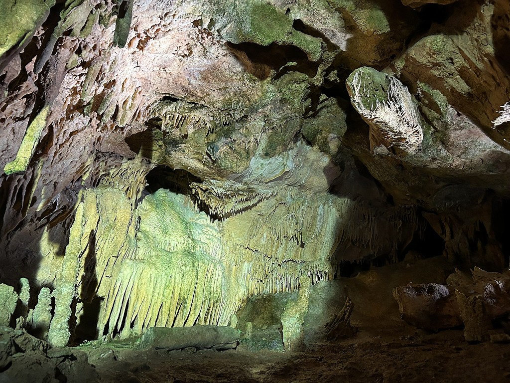 Interior of a cave featuring various stalactites and stalagmites, illuminated by a spotlight, showcasing intricate rock formations.