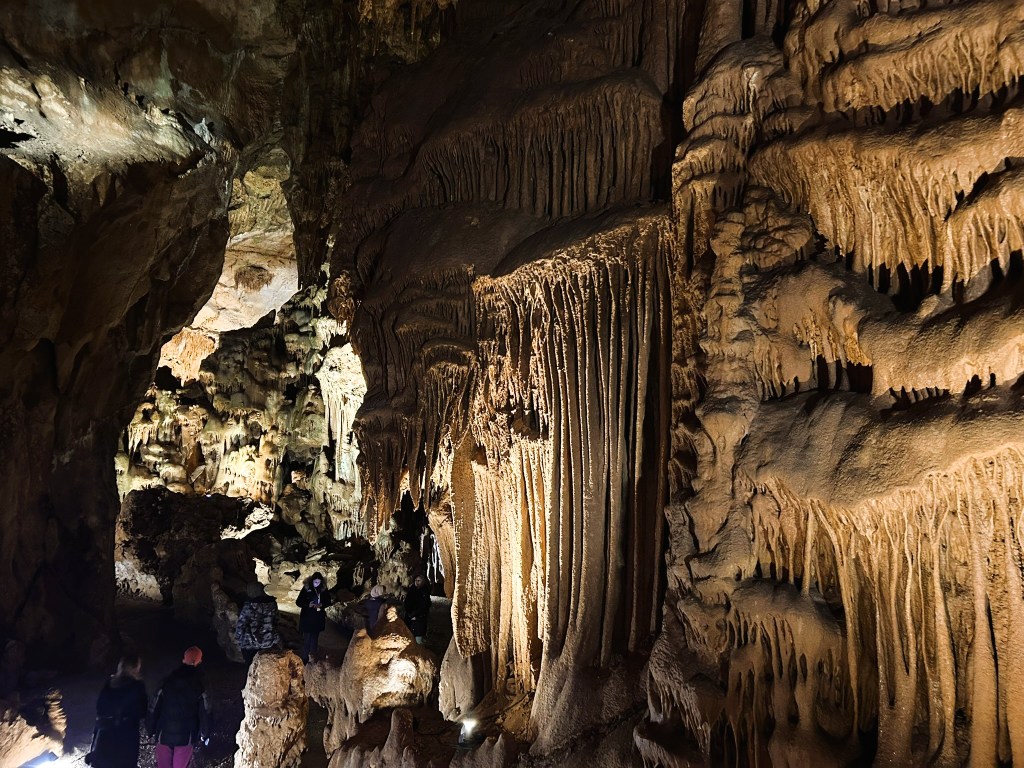 Interior of a cave featuring stunning rock formations, stalactites and stalagmites, with visitors exploring the illuminated pathways.
