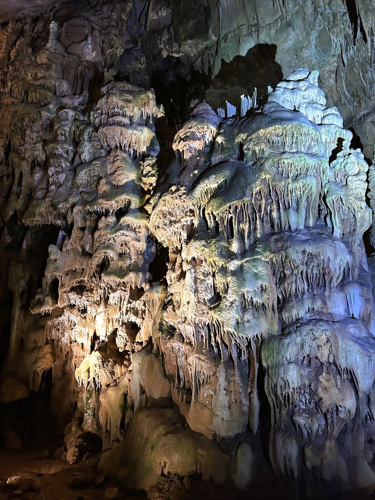 Intricate limestone formations inside a cave, illuminated by soft lighting, showcasing stalactites and stalagmites.