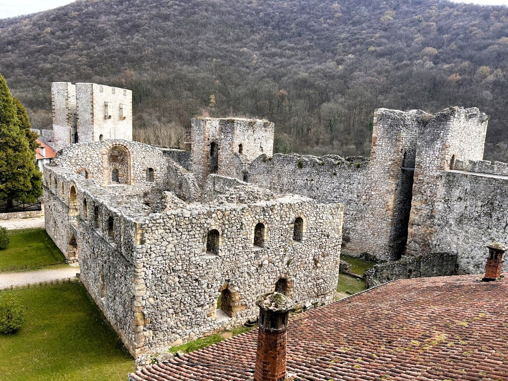 Aerial view of the ruins of a stone castle surrounded by trees and hills.