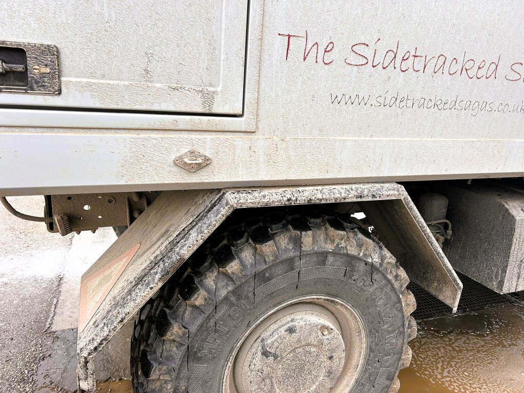 Close-up of a dirty side panel and tyre of a vehicle belonging to Sidetracked Gas, with visible wear and mud.