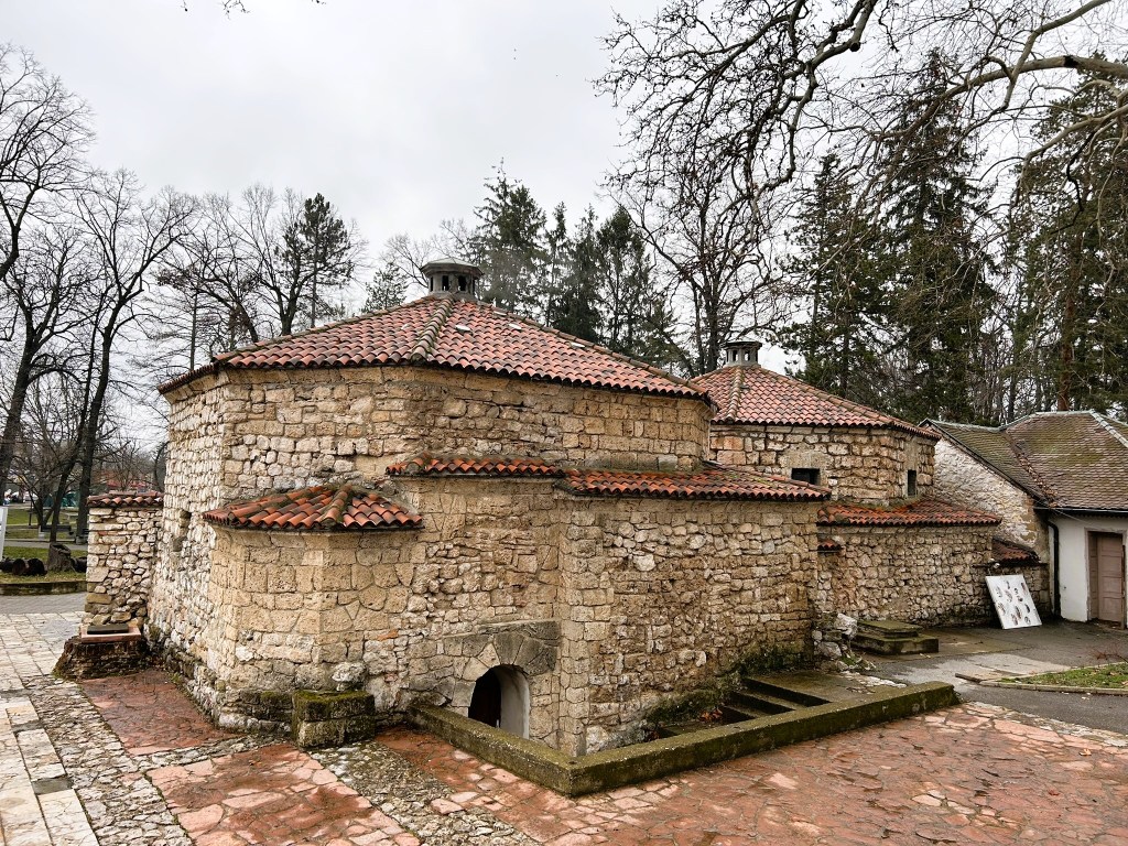 Historic stone building with a tile roof, surrounded by bare trees and a stone path.